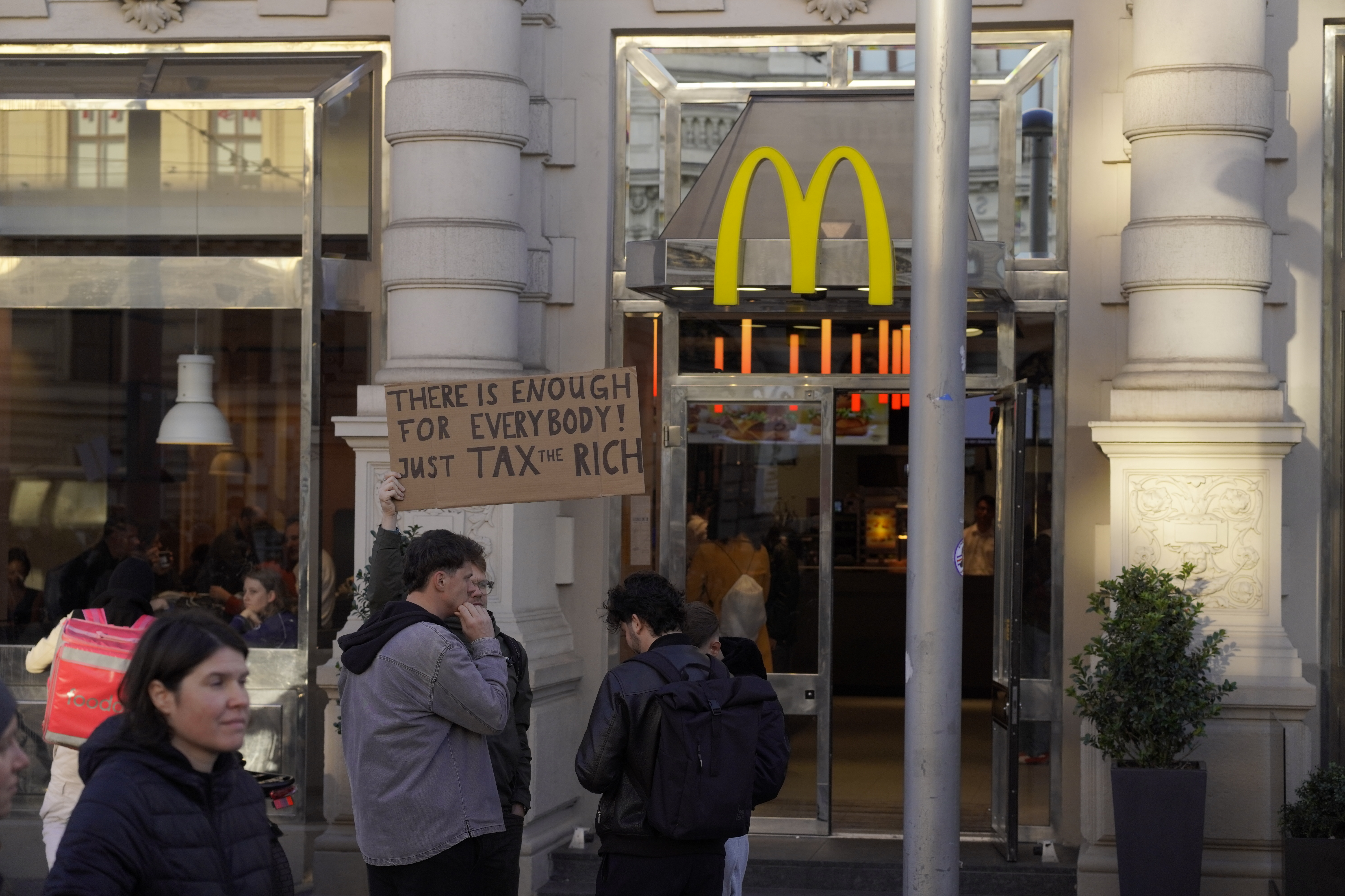 Demo Plakat mit Aufschrift There is enough for everyone. Just TAX THE RICH. Vor einer McDonalds Filliale